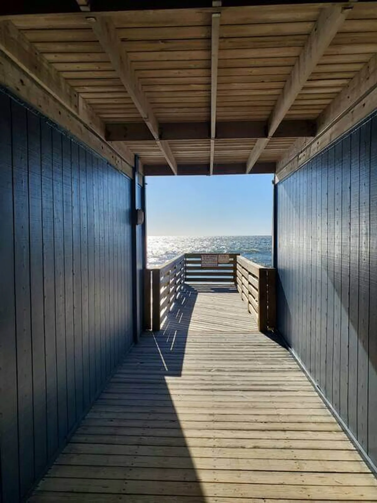 This image features a wooden walkway with a clear view of the ocean, highlighted by natural light and tranquil surroundings. The pathway leads from the community area toward the beach, visually connecting residents with direct beach access.