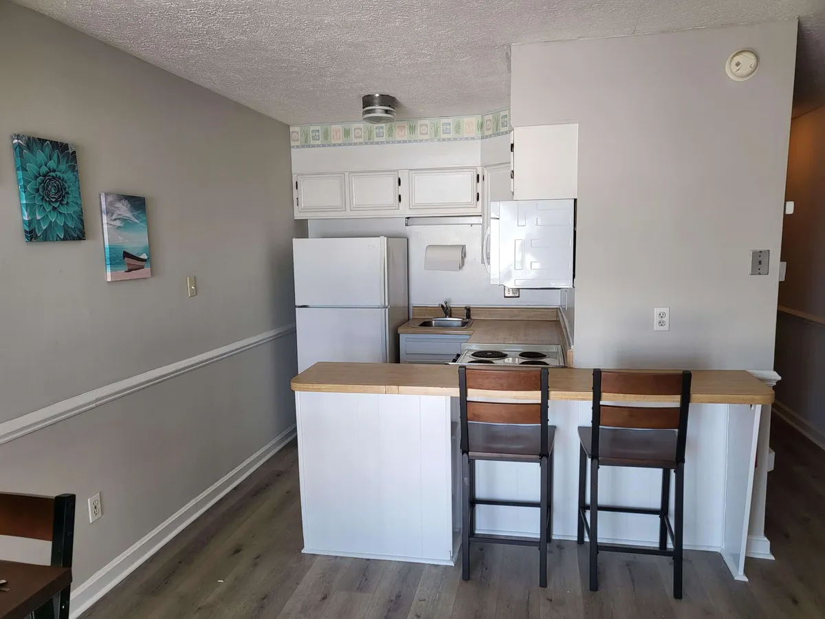This image captures a warm and welcoming kitchen scene featuring a stylish kitchen counter with stools, a modern refrigerator, and tasteful wall art. The arrangement is ideal for both meal preparation and casual dining, highlighting the kitchen's social and functional aspects.