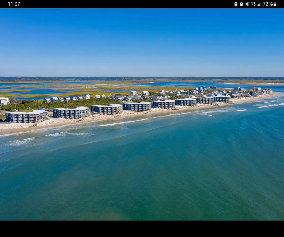 A wide exterior view of the beachfront properties facing the expansive blue ocean under a clear sky. The shoreline is visible and suggests easy access from the condos, with a relaxing and open ambiance ideal for families.