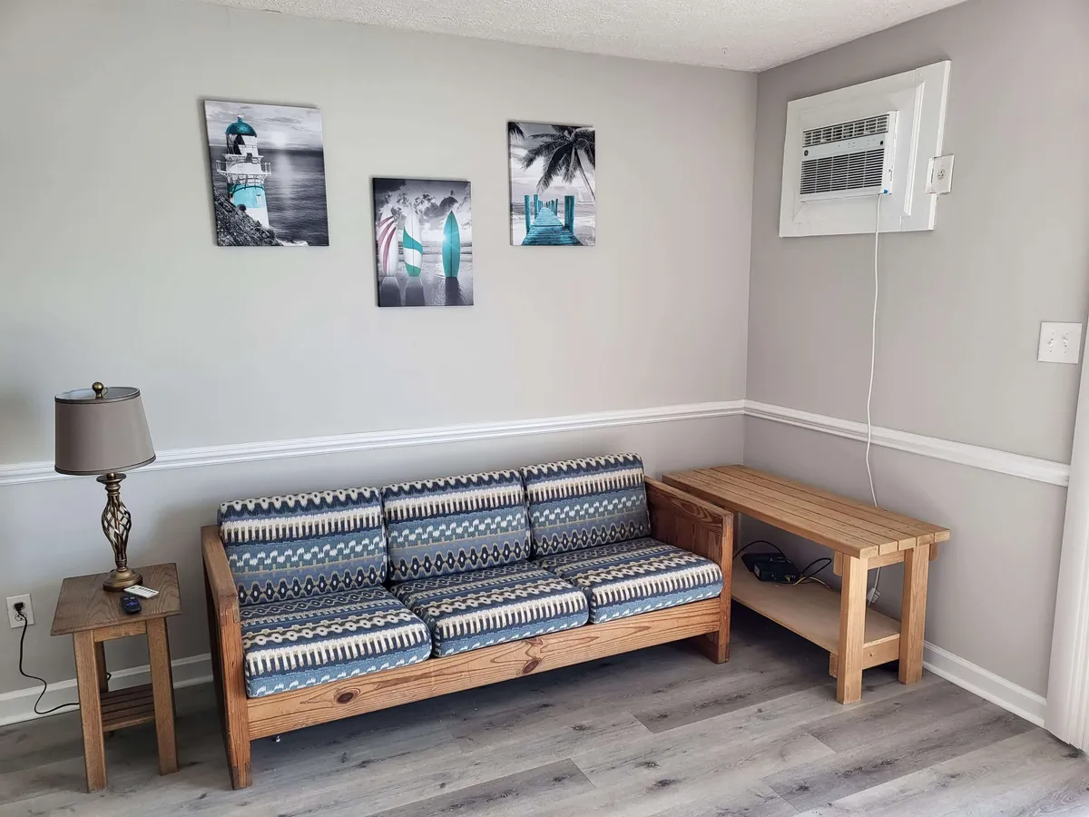 A cozy living area with a sofa, wall artwork, a lamp, and a side table creates a welcoming space for relaxation. The scene is warm and comfortable, ideal for indoor enjoyment during any season or tide.
